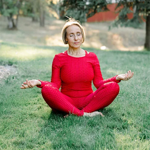 Kasia sitting on grass in Lotus position in red yoga liatards