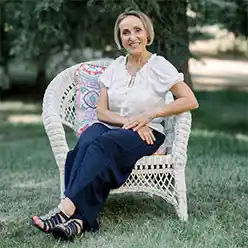 Kasia seated in a white wicker chair outside on a lawn surrounded by trees